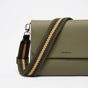 Peut inclure: Un sac à bandoulière en cuir vert avec une bandoulière rayée jaune et bleu marine. Le sac a une fermeture à rabat et le nom de la marque "PAMPUS" est embossé sur le devant.