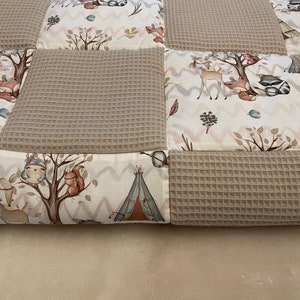 May include: A beige and white patchwork quilt with a woodland animal theme. The quilt features a variety of animals, including deer, squirrels, owls, and raccoons. The quilt is made of a soft, comfortable fabric and is perfect for cuddling up on the couch.