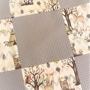 Op de afbeelding: Een patchwork babydeken met een bosdieren thema. De deken is gemaakt van zacht, gestructureerd stof in grijstinten en cr&egrave;me. Het ontwerp bevat een verscheidenheid aan dieren, waaronder herten, konijnen, uilen en wasberen, evenals bomen, paddenstoelen en andere bosselementen.
