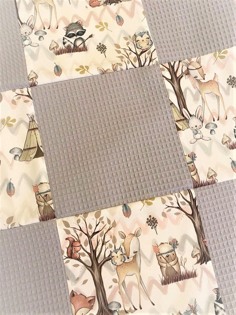 Op de afbeelding: Een patchwork babydeken met een bosdieren thema. De deken is gemaakt van zacht, gestructureerd stof in grijstinten en cr&egrave;me. Het ontwerp bevat een verscheidenheid aan dieren, waaronder herten, konijnen, uilen en wasberen, evenals bomen, paddenstoelen en andere bosselementen.