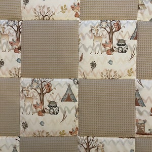 May include: A beige and white patchwork quilt with a woodland animal theme. The quilt features a variety of animals, including deer, raccoons, foxes, and owls. The quilt is made of a soft, comfortable fabric and is perfect for cuddling up on the couch.