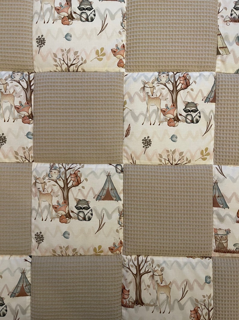 May include: A beige and white patchwork quilt with a woodland animal theme. The quilt features a variety of animals, including deer, raccoons, foxes, and owls. The quilt is made of a soft, comfortable fabric and is perfect for cuddling up on the couch.