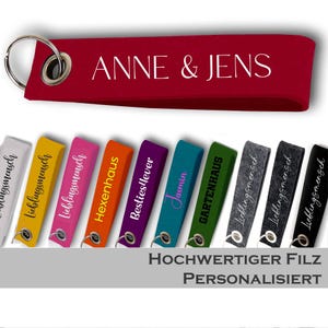 Könnte beinhalten: Eine Sammlung rechteckiger Filz-Schlüsselanhänger in verschiedenen Farben wie Rot, Gelb, Pink, Orange, Lila, Türkis, Grün, Grau und Schwarz. Jeder Schlüsselanhänger hat einen Metallring und ist mit weißem oder schwarzem Text personalisiert.