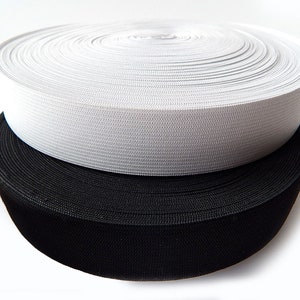 Könnte beinhalten: Zwei Rollen elastisches Band, eine weiße und eine schwarze, übereinander gestapelt. Die Rollen sind eng gewickelt und zeigen die Textur des Stoffes. Die weiße Rolle liegt auf der schwarzen, was einen Kontrast erzeugt.