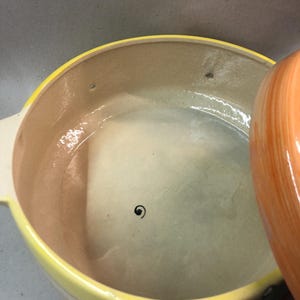 May include: A yellow ceramic casserole dish with a lid. The dish has a brown interior and a colorful design of birds and frogs around the rim.