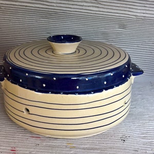 May include: A white ceramic casserole dish with a blue and white patterned lid. The lid has a circular design with white dots on a blue background. The dish has a striped design with blue lines on a white background.