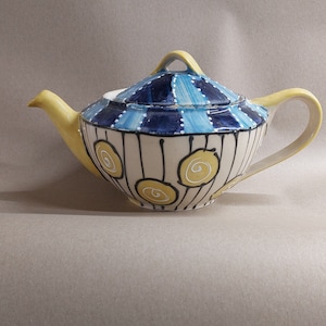 May include: A yellow teapot with a blue and white striped design and yellow swirl accents. The teapot has a lid and a spout.
