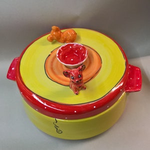 May include: Yellow ceramic container with a red lid and white polka dots. The lid has a small red bowl and two small ceramic animal figurines, one orange and one red.