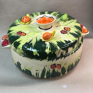 May include: A ceramic casserole dish with a green and white floral design. The lid has a small bowl in the centre and is decorated with small ceramic snails and turtles.