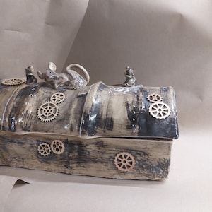 May include: A handcrafted ceramic box with a rustic, steampunk aesthetic. The box is painted in shades of brown and black, with wooden gear accents. Three small mouse figurines are perched on top. The box measures approximately 25 cm long.