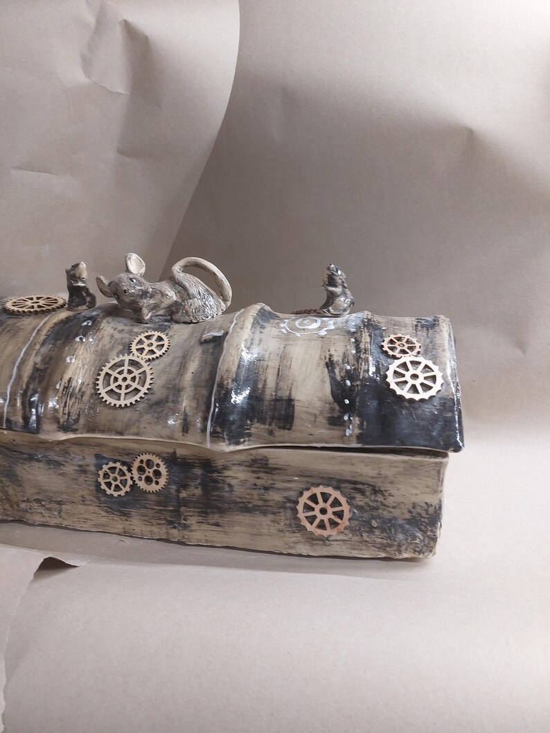 May include: A handcrafted ceramic box with a rustic, steampunk aesthetic. The box is painted in shades of brown and black, with wooden gear accents. Three small mouse figurines are perched on top. The box measures approximately 25 cm long.