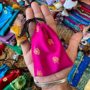 May include: A small pink drawstring bag with gold floral patterns. The bag is made of silk and has a black drawstring.