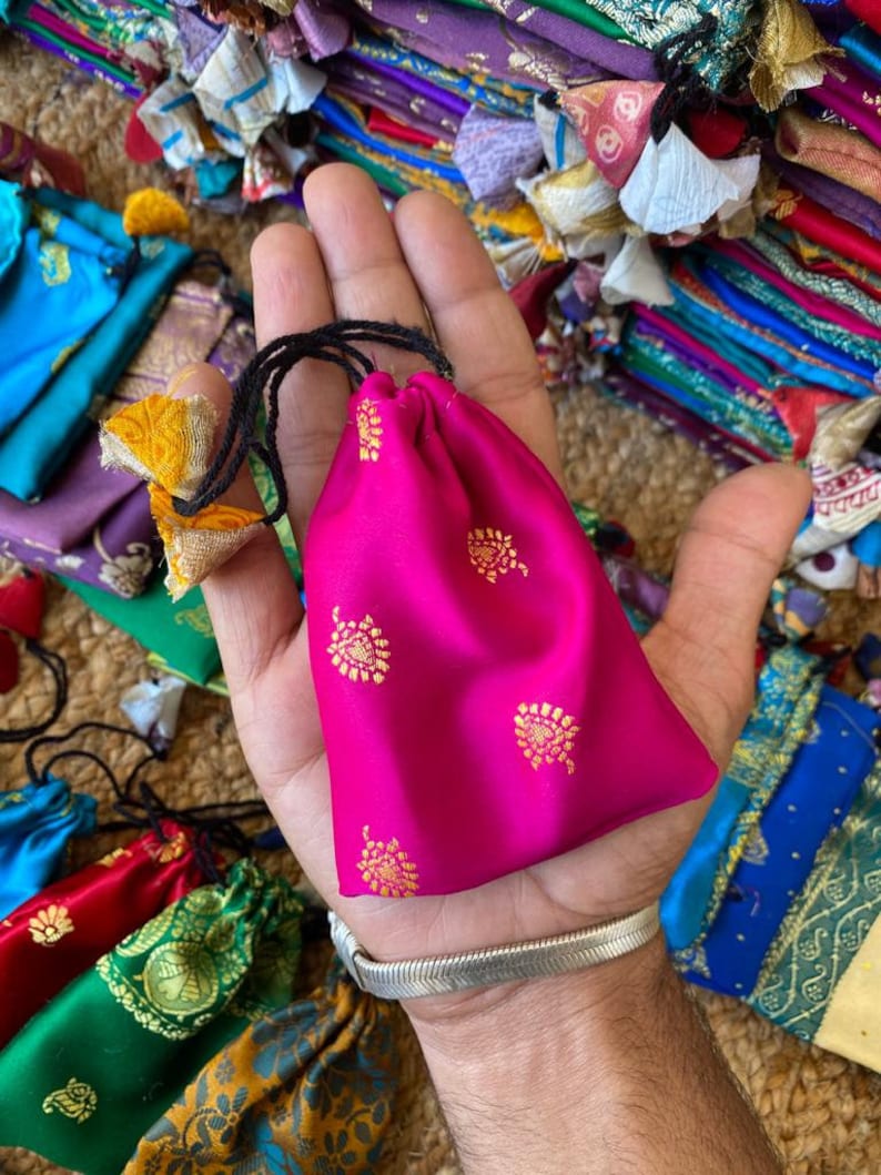 May include: A small pink drawstring bag with gold floral patterns. The bag is made of silk and has a black drawstring.