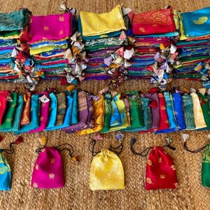 May include: A collection of colorful fabric pouches with drawstrings. The pouches are made of various fabrics, including silk, cotton, and velvet. They are decorated with intricate embroidery and patterns. The pouches are arranged in a row on a woven surface.