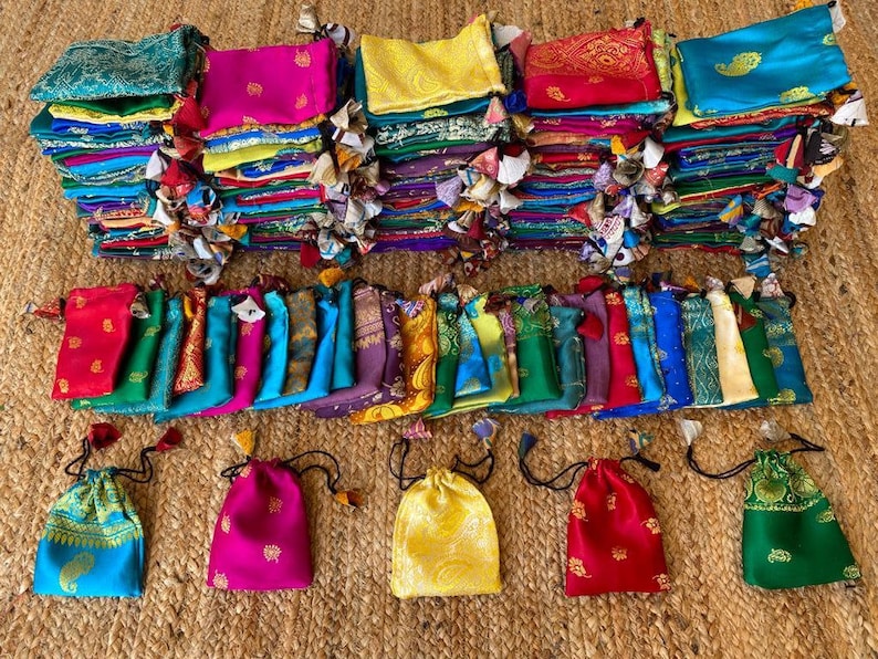 May include: A collection of colorful fabric pouches with drawstrings. The pouches are made of various fabrics, including silk, cotton, and velvet. They are decorated with intricate embroidery and patterns. The pouches are arranged in a row on a woven surface.
