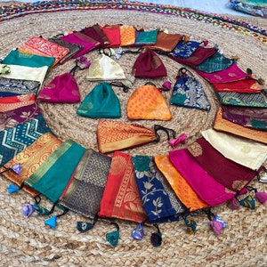 May include: A collection of colorful fabric pouches with tassels. The pouches are made of various fabrics with intricate patterns and gold accents. They are arranged in a circle on a woven mat.
