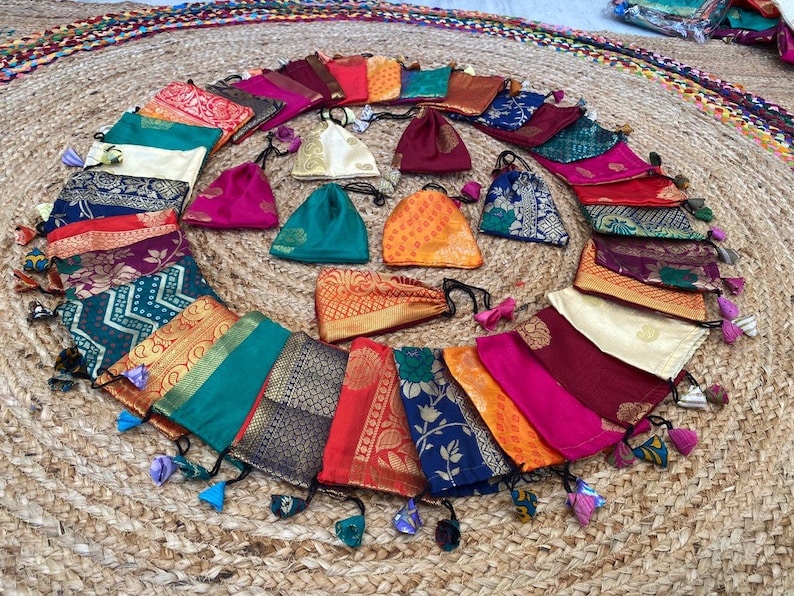May include: A collection of colorful fabric pouches with tassels. The pouches are made of various fabrics with intricate patterns and gold accents. They are arranged in a circle on a woven mat.