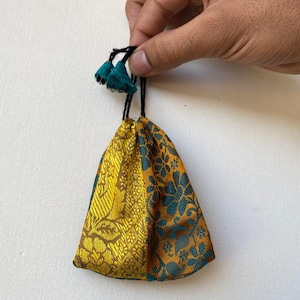 May include: A small, drawstring pouch with a gold and teal floral pattern. The pouch has a black drawstring with teal tassels.