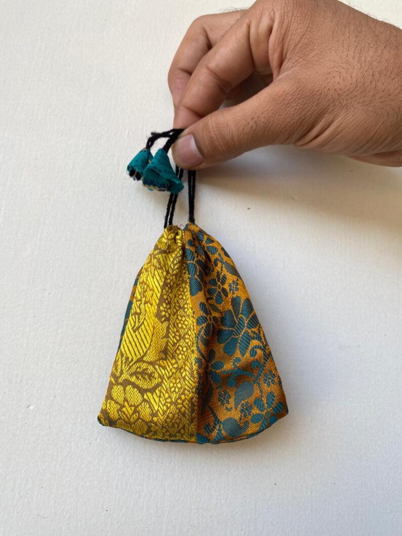 May include: A small, drawstring pouch with a gold and teal floral pattern. The pouch has a black drawstring with teal tassels.