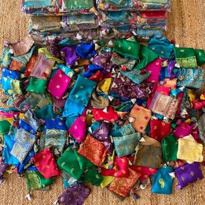 May include: A large pile of colorful small fabric pouches with gold embroidery. The pouches are made from a variety of fabrics, including silk, velvet, and brocade. They are all tied with a small tassel.