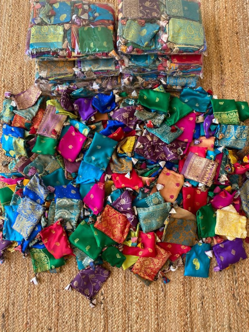 May include: A large pile of colorful small fabric pouches with gold embroidery. The pouches are made from a variety of fabrics, including silk, velvet, and brocade. They are all tied with a small tassel.