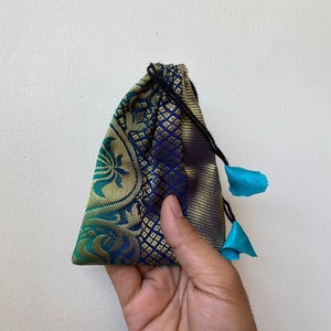 May include: A small blue and green drawstring bag with gold accents and turquoise tassels. The bag is made of a patterned fabric.