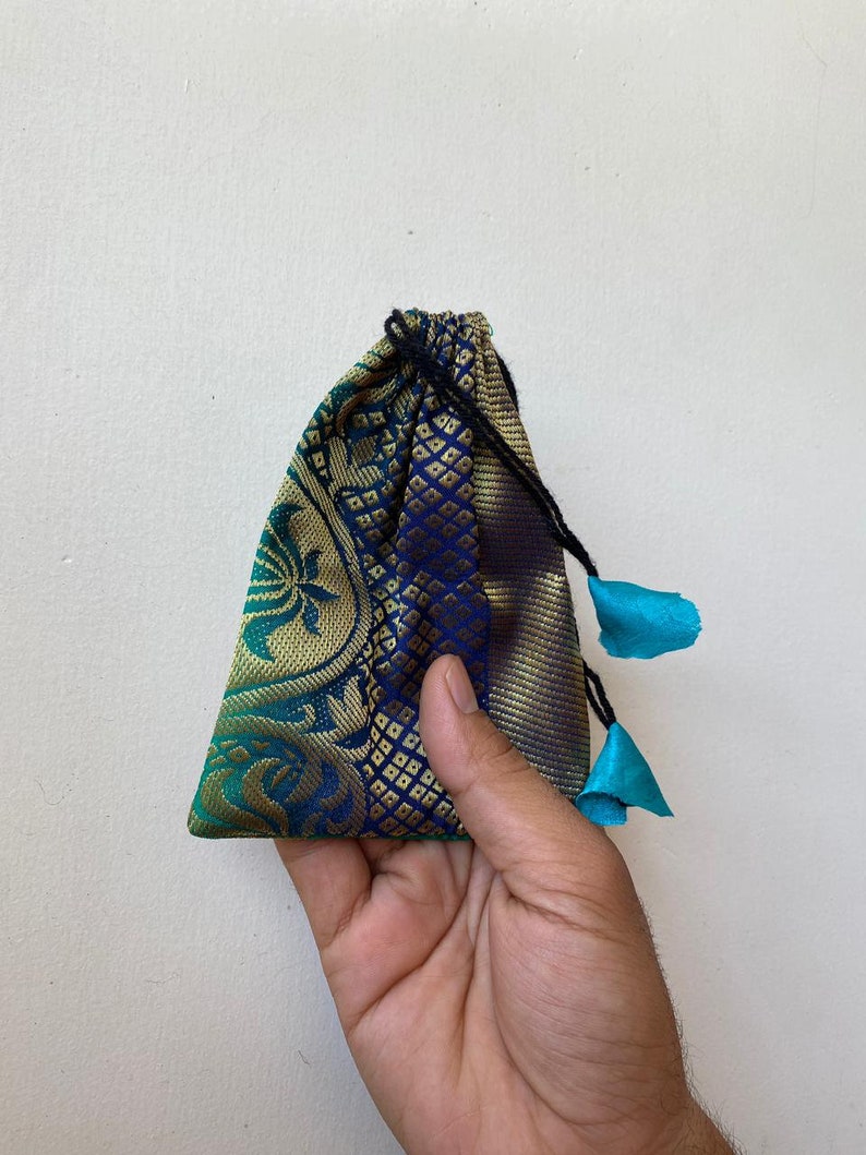 May include: A small blue and green drawstring bag with gold accents and turquoise tassels. The bag is made of a patterned fabric.