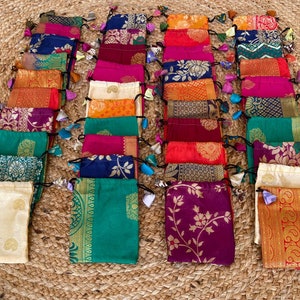 May include: A collection of 20 small, colorful drawstring bags made from fabric with intricate patterns. The bags are arranged in rows and have tassels on the drawstrings.