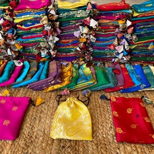 May include: A stack of colorful fabric pouches with intricate designs. The pouches are arranged in a pyramid shape and are made of silk or satin. There are several pouches in the foreground, with a variety of colors and patterns.