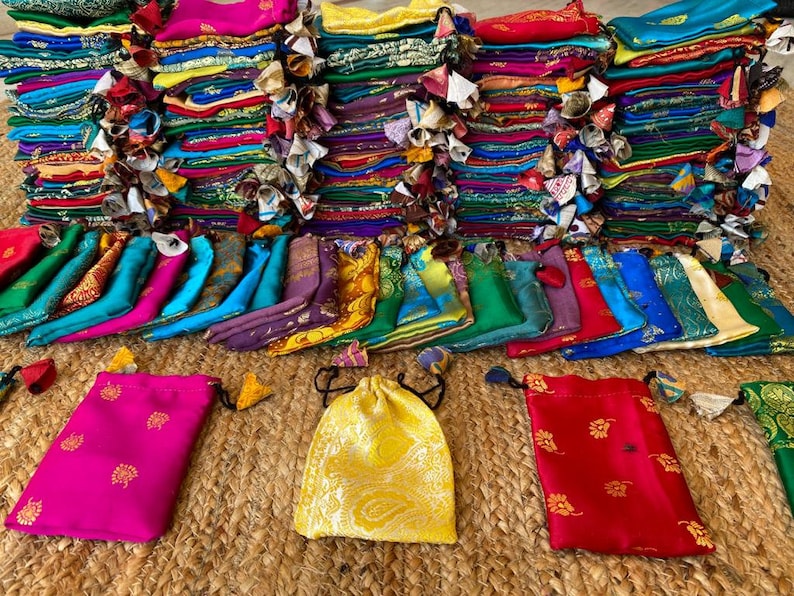 May include: A stack of colorful fabric pouches with intricate designs. The pouches are arranged in a pyramid shape and are made of silk or satin. There are several pouches in the foreground, with a variety of colors and patterns.