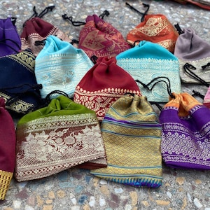 Peut inclure: Une collection de pochettes à cordon colorées dans diverses teintes, dont le turquoise, le violet et l'or. Les pochettes présentent des bordures et des accents dorés et argentés à motifs complexes. Chaque pochette a une fermeture à cordon noire.