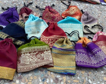 May include: A collection of colorful drawstring pouches in various shades, including teal, purple, and gold. The pouches feature intricate gold and silver patterned borders and accents. Each pouch has a black drawstring closure.