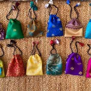 May include: A collection of 12 small drawstring bags made of colorful patterned fabric. The bags are all different colors and patterns, including green, blue, purple, red, yellow, and gold. The bags are all about 4 inches in diameter and have a drawstring closure.