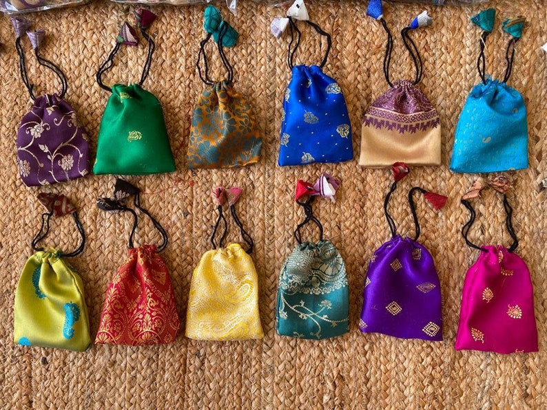 May include: A collection of 12 small drawstring bags made of colorful patterned fabric. The bags are all different colors and patterns, including green, blue, purple, red, yellow, and gold. The bags are all about 4 inches in diameter and have a drawstring closure.