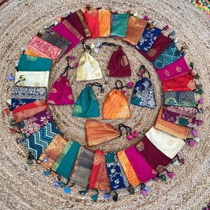 May include: A collection of 20 small, colorful fabric pouches with drawstrings and tassels. The pouches are arranged in a circle on a woven rug.