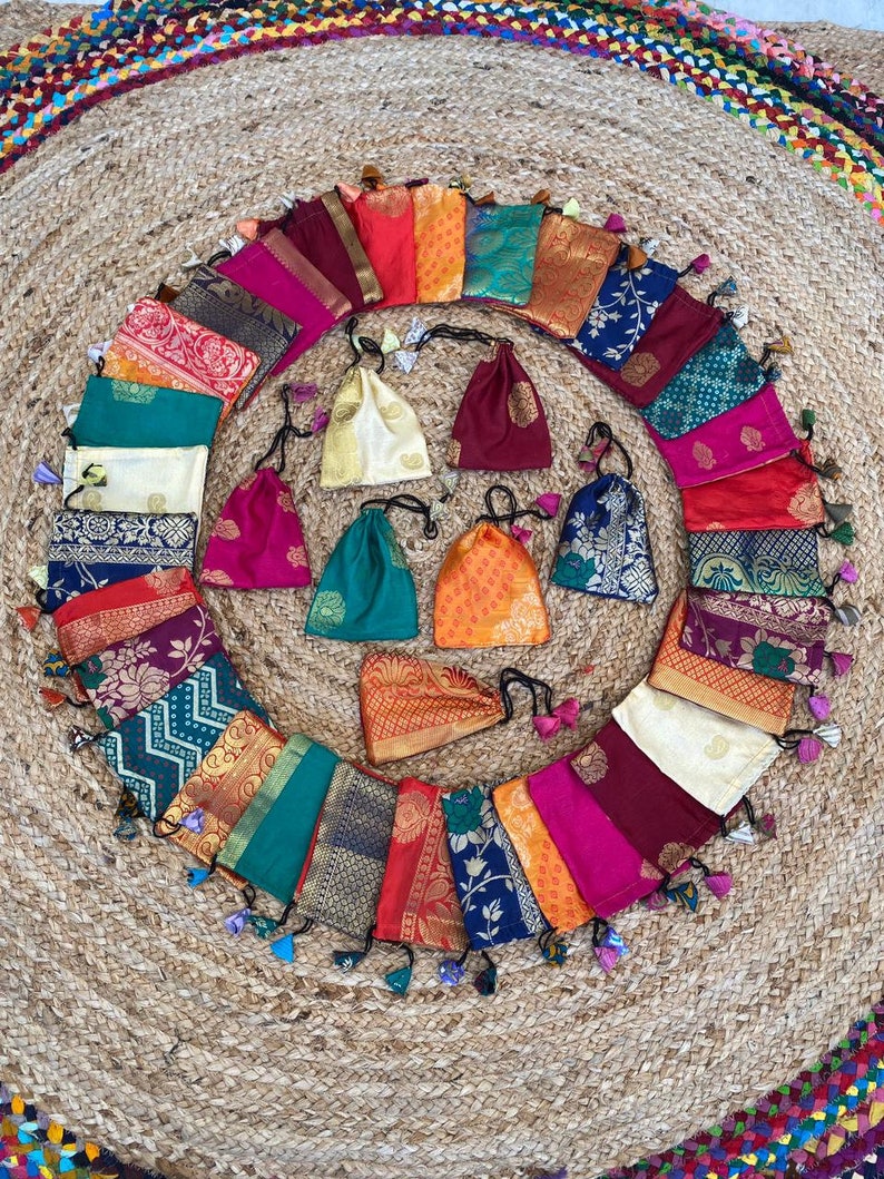 May include: A collection of 20 small, colorful fabric pouches with drawstrings and tassels. The pouches are arranged in a circle on a woven rug.