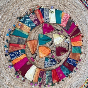 May include: A collection of 20 colorful fabric pouches with tassels. The pouches are arranged in a circle on a woven rug. The pouches are made of different fabrics, including silk, cotton, and velvet. They are decorated with various patterns, including floral, geometric, and paisley.