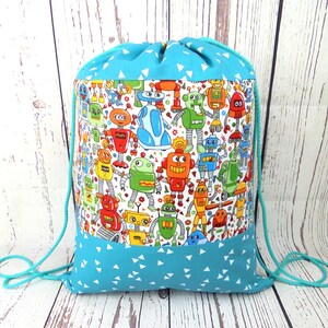 Peut inclure: Un sac à cordon de serrage avec un motif de robots colorés sur fond blanc. Les sections supérieure et inférieure sont turquoise avec des motifs triangulaires blancs. Il a des cordons de serrage turquoise.