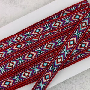 Könnte beinhalten: Roter und blauer gemusterter Besatz mit geometrischem Design. Der Besatz ist um eine weiße Karte gewickelt.