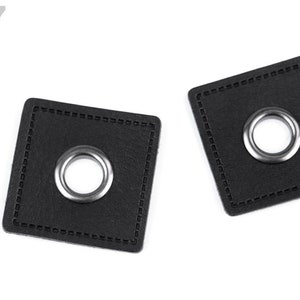 Könnte beinhalten: Zwei schwarze Lederquadrate mit einem silbernen Metallösen in der Mitte. Die Quadrate haben einen genähten Rand.
