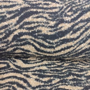 Op de afbeelding: Close-up van een stof met een zebra streep patroon. De stof heeft een getextureerd, gelust oppervlak. De strepen zijn een combinatie van marineblauw en bruin, waardoor een gedurfd dierenprintontwerp ontstaat. De stof wordt waarschijnlijk gebruikt voor bekleding of mode.