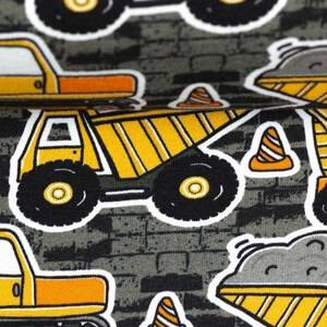 Puede incluir: Una tela gris con un patr&oacute;n repetido de veh&iacute;culos de construcci&oacute;n amarillos y negros, incluyendo camiones de volteo, camionetas y conos de tr&aacute;fico.