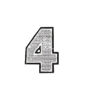 Könnte beinhalten: Ein Bügelbild in Form der Zahl vier, aus silbernen Pailletten mit schwarzem Umriss.
