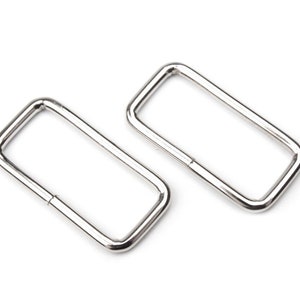 Könnte beinhalten: Zwei silberne D-Ringe aus Metall, jeweils mit rechteckiger Form und glatter, polierter Oberfläche.