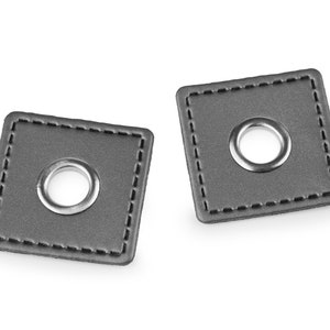 May include: Two grey leather grommets with silver metal rings. The grommets have a stitched border.