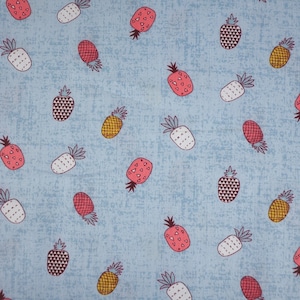 Op de afbeelding: Een blauwe stof met een herhalend patroon van roze, witte en gele ananas. De ananas zijn op een eenvoudige, gestileerde manier getekend.