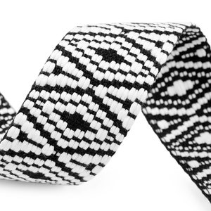 Op de afbeelding: Zwart-wit geweven lint met een geometrisch patroon. Het lint is gekruld en heeft een textuur.