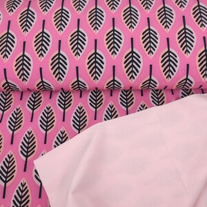 Op de afbeelding: Roze stof met een zwart-wit bladmotief. De stof is dubbelgevouwen, waardoor een effen roze onderkant zichtbaar wordt.