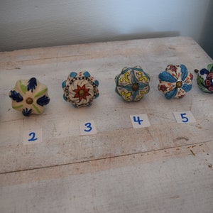 Peut inclure: Six boutons de tiroir en céramique avec des motifs floraux colorés. Les boutons sont numérotés de 1 à 6.