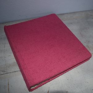 Może przedstawiać: Prostokątny, różowy segregator pokryty tkaniną. Segregator ma teksturowaną powierzchnię i widoczny grzbiet. Okładka ma jednolity, żywy różowy kolor. Segregator jest zamknięty i wydaje się nowy.